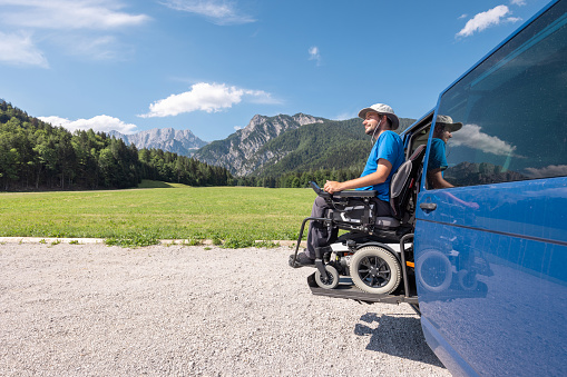 Young Caucasian man in a wheelchair using the vertical platform lift to get in the van parked in the nature