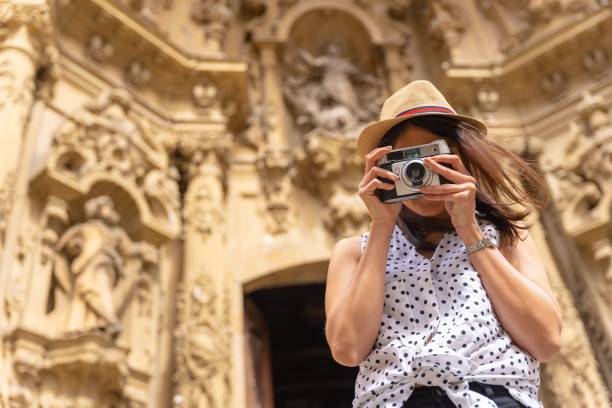 帽子をかぶったヒスパニック系の女性が街を訪れ、ビンテージカメラで写真を撮る - casual cheerful looking at camera outdoors ストックフォトと画像