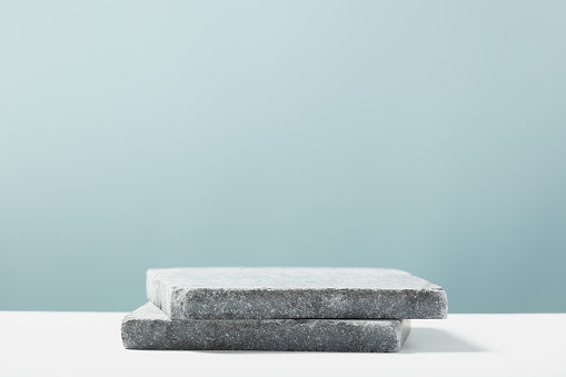 Flat granite pedestal on blue background. Stone stand for natural design concept. Horizontal image, center composition, hard light, front view
