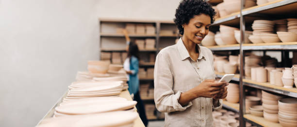istock Smiling ceramist using a smartphone in her shop 1455216617