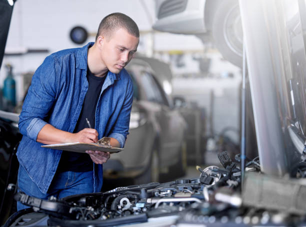 istock Car service, inspection and mechanic by car with clipboard checking engine. Technician, engineer and man working in garage or workshop writing notes for repair, maintenance and motor care for vehicle 1455222281