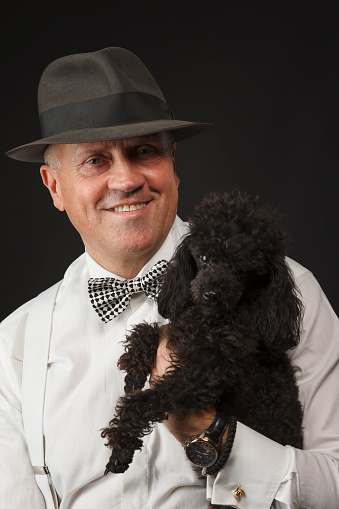 Pet love. Vintage portrait of a senior man with dog, black miniature poodle. Friendship, Black - dark background.