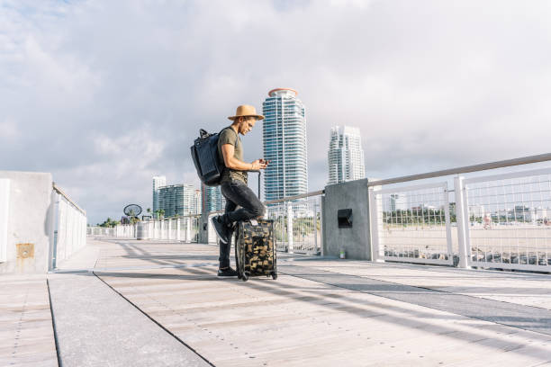 un jeune homme portant un chapeau, une valise et un sac à dos cherche son chemin sur le téléphone. - leaving business landscape men photos et images de collection