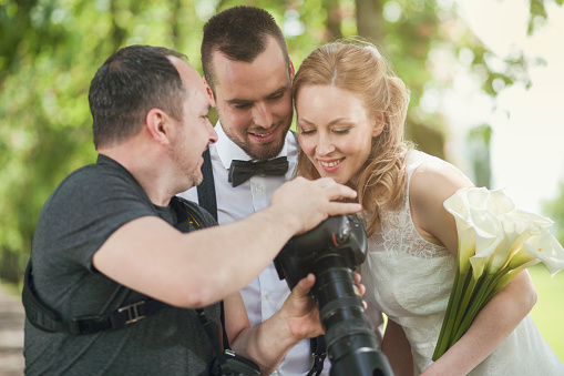 Wedding photographer showing photos on his camera to the newlywed couple in nature.