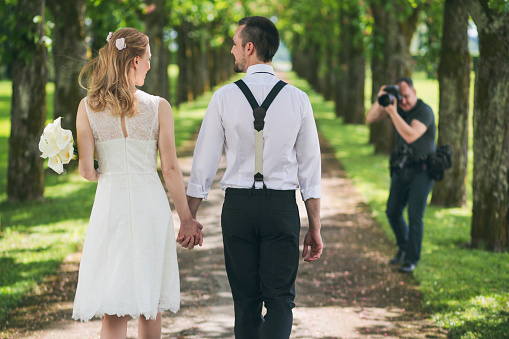 Bride and groom walking in tree-lined path with a photographer in front.