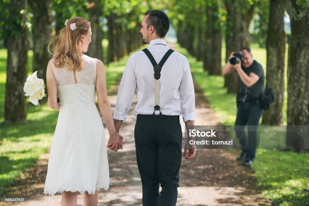 Wedding photoshoot Bride and groom walking in tree-lined path with a photographer in front. 20-29 Years Stock Photo