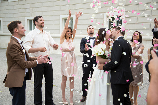 Wedding ceremony ending with couple kissing and guests throwing rose petals on them.