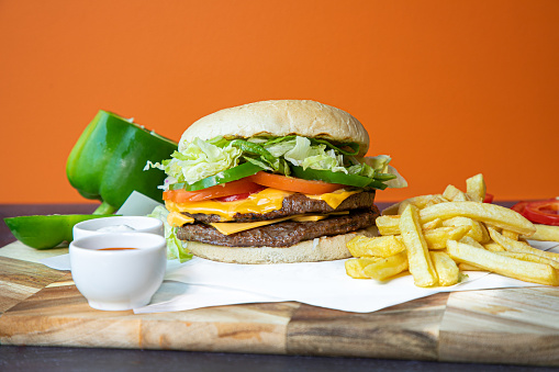 Cheese Burger with Chips on a wooden chopping board with an orange background