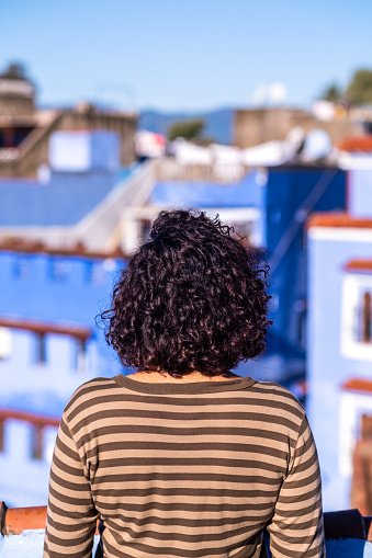 Woman with her back to the view from the terrace of a tourist enclave of blue houses.