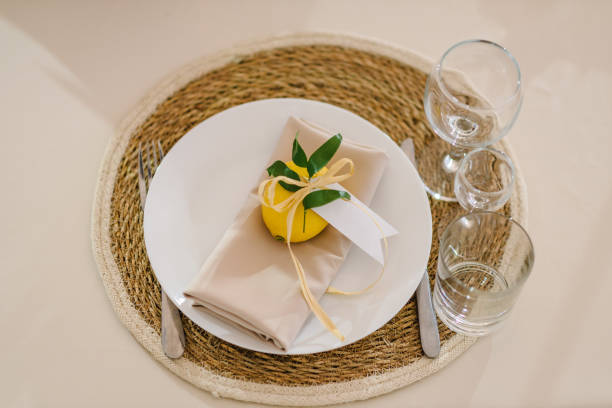 istock Banquet table served with silverware, plates with napkins, cutlery and glasses. Serving, setting table. Gift citrus lemons decorated with ribbons and branch greenery. Compliment for guests. Reception. 1455232343