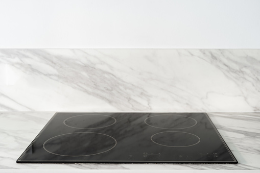 closeup of empty electrical glass ceramic hob with sensor buttons on control panel built in marble countertop and white wall background with copy space