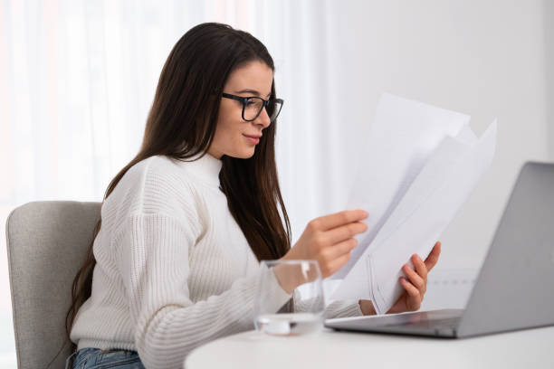 istock Smiling young businesswoman in glasses looking at the documents and check with notebook 1455232576