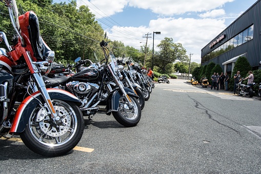 Nashua, United States – October 08, 2015: Harley Davidson motorcycles parked on the street and motorcyclists chatting in the background on a sunny day, with green trees along the street