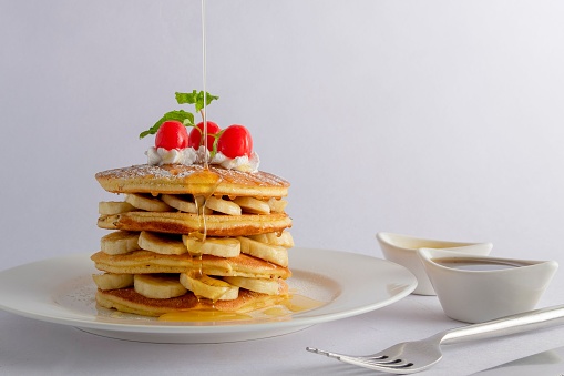 A closeup of pancakes with banana and cherry creamy topping served with dripping honey