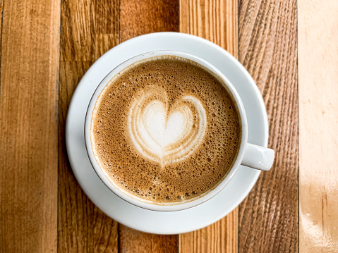 A mug of flat white coffee, latte, cappuccino on a wooden background. Coffee art. Heart flower shape latte art