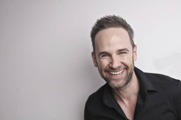 istock Handsome Italian man wearing a black shirt standing against a white wall and laughing 1455234708