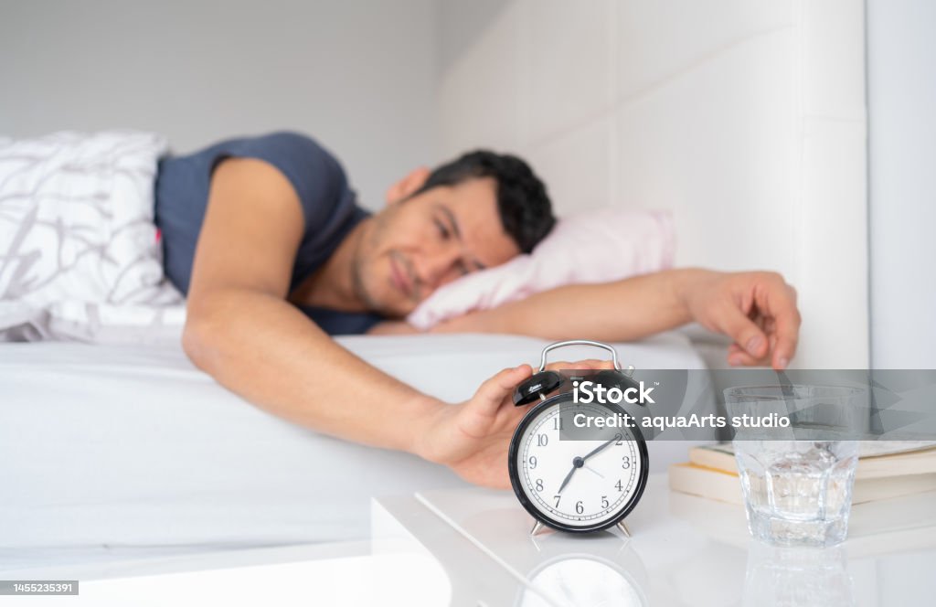 Young Man Reaching For Her Alarm Clock After Waking Up İn Bed At Home Young Man Waking Up İn Her Bed Early İn The Morning And Reaching For Her Alarm Clock Adult Stock Photo