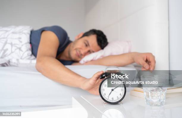 Young Man Reaching For Her Alarm Clock After Waking Up İn Bed At Home Stock Photo - Download Image Now