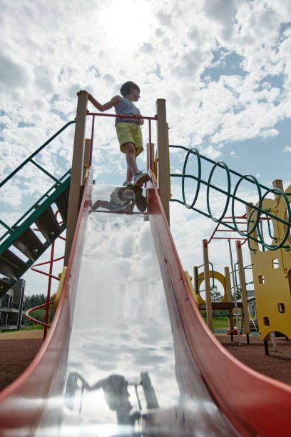 istock Young boy standing on top of slide against sky 1455235460