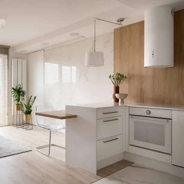 Photo of Small white kitchen open to room with marble wall