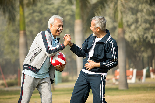 Two laughing old male friends with ball at park