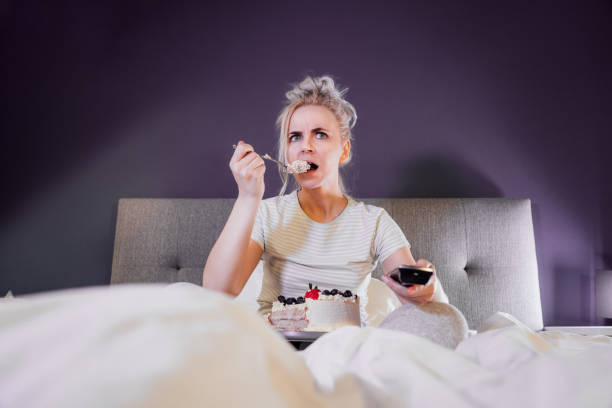 istock Emotionally stressed, shocked woman eating cake and holding a remote control while watching TV in bed. Scary horror movie or terrible news, scare in her eyes Overeating, Jamming of negative emotions 1455237377