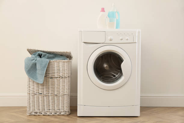 istock Laundry room interior with modern washing machine and wicker basket near white wall 1455242804