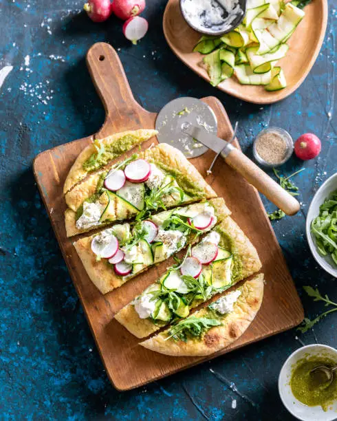 A top view of vegetarian focaccia bread with radish, courgette, rocket, cheese and pesto