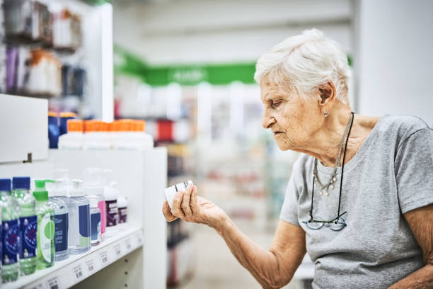 senior woman reading label of medicine in pharmacy - 96 well imagens e fotografias de stock