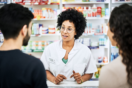 Caucasian pharmacist scrolling on digital tablet reviewing cold and flu medication to mixed race patient standing in drugstore pharmacy . High quality photo