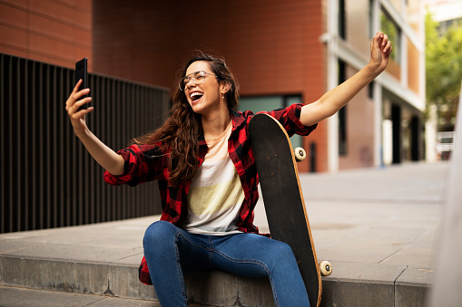 Beautiful woman with skateboard. Young urban girl using the phone outside.