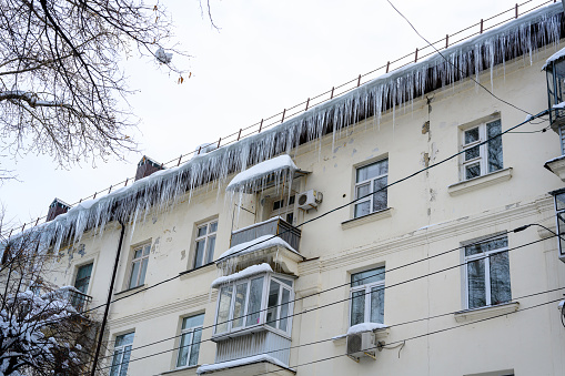 Big icicles above the entrance to a residential building. Hanging icicles above the entrance to a building, risk to life. Sharp icicles hang from the roof of an old apartment building.