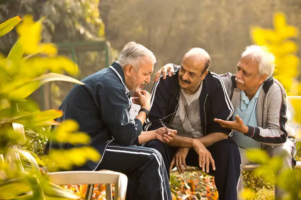 Photo of Depressed old man with friends sitting at park