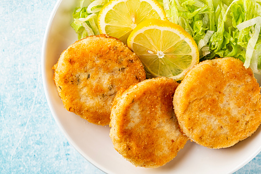 Top view of Fish cakes or burger, or cutlets. Made from ground perch and tuna with herbs, breaded and fried, served with iceberg salad, lemon slices.