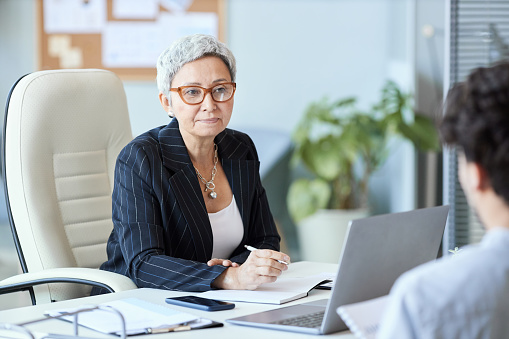 Portrait of mature businesswoman wearing glasses talking to employee in meeting, copy space