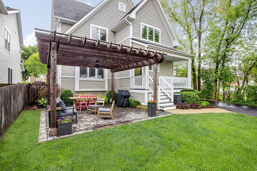 Elmhurst, IL, USA - May 22, 2019:  A backyard brick patio with lots of seating, a grill, and a wooden pergola over the top of a luxurious home.