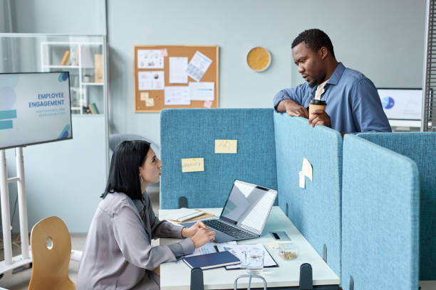 istock Two young colleagues talking over cubicle wall in office 1455250070
