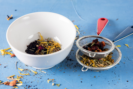 Bowl of Healthy Herbal Tea with Dried Berry and Camomile Flowers Two Strainer with Herbal Tea on Blue Background