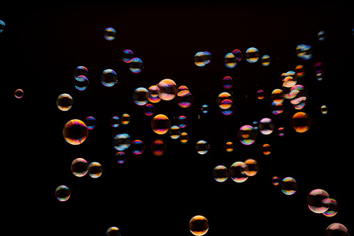 Many soap bubbles in different colors and sizes on black background, studio shot