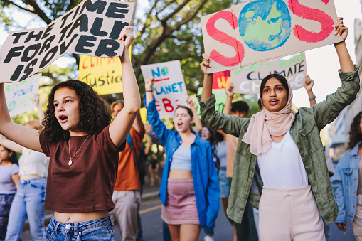 Group of youth activists standing up against climate change and global warming. Multicultural young people protesting with posters and banners. Diverse teenagers joining the global climate strike.