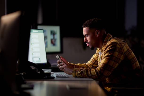istock Businessman Working Late In Office With Face Illuminated By Computer Screen Using Mobile Phone 1455261361