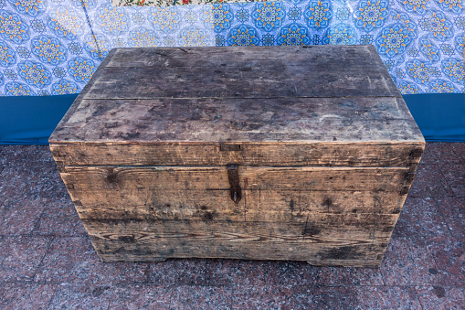 Antique grunge wooden scratched chest with a metal lock. Very old, aged wooden chest with rusty steel lock on blue fabric background.