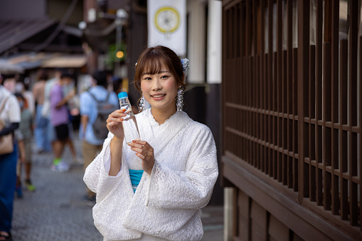 Woman in white summer kimono holding 'Ramune' soda pop on traditional Japanese shopping street