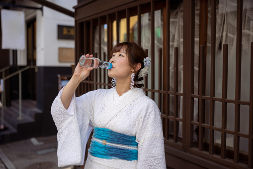 Woman in white summer kimono drinking 'Ramune' soda pop on traditional Japanese shopping street