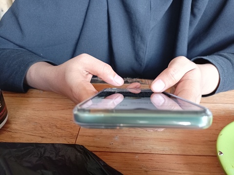 An Asian Muslim woman playing on a cell phone