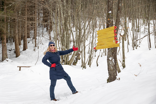 Shot of an adult woman in the forest wondering where to go on a snowy day outdoors. Woman standing near tourist information signs and trying to decide where to go. Choice concept. Copy space.