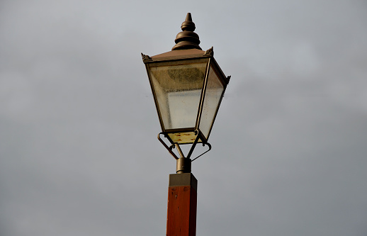 Historicizing style of lamp that is not gas but LED lights. Lantern frame without glass filling. historic city center with natural facade brown wooden windows with arch, lamppost, reminiscing