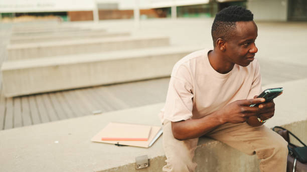 istock Young african student sits outside of university, uses cellphone, taps on smartphone screen 1455272913
