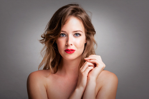 Headshot of gorgeous young woman with perfect skin and make-up posing at isolated grey background with copy space. Beautiful female wearing red lipstick.