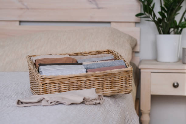 istock Wicker container with clothes on the bed. Vertical clothing storage. Concept of minimalism lifestyle 1455275421